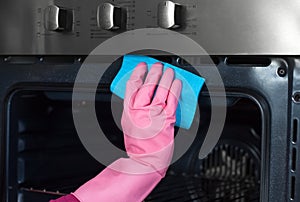 woman hand in protective glove with rag cleaning oven at home kitchen