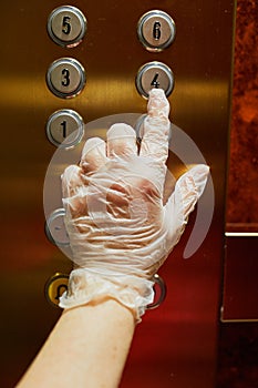 Woman hand in protective single use glove presses elevator button