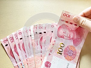 Woman hand pull one hundred Chinese yuan money from stacking on yellow background.