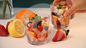 Woman hand put glass of red wine fresh sangria or punch with fruits and berries on the table