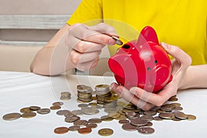 Woman hand put money coins in a piggy bank for saving money and financial concept, several coins on the table