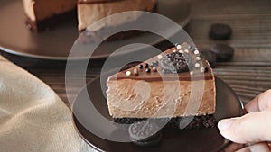 Woman hand put a plate with chocolate cheese cake on the wooden table.