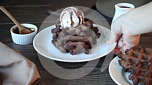 Woman hand put on the table plate with homemade chocolate waffles with ice cream decorated chocolate syrup.