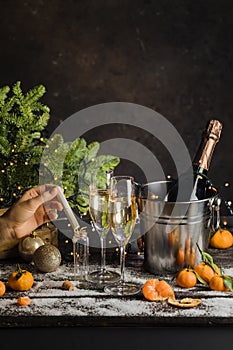 woman hand puts Christmas wish in little glass bottle. Champagne in metal bucket behind. Two glasses