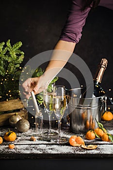 woman hand puts Christmas wish in little glass bottle. Champagne in metal bucket behind. Two glasses