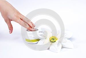 Woman hand puts his finger in a bowl of cream for the face and white flower beside box