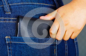 Woman hand putting a black wallet inside of jeans back pocket