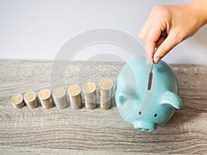 Woman hand putting coin into blue piggy bank with coins pile growth graph, saving money for future investment plan and retirement