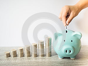 Woman hand putting coin into blue piggy bank with .coins pile growth graph, saving money for future investment plan and retirement