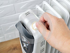 Woman hand putting a coin into home electric oil heater. The concept of higher electricity costs during the cold season