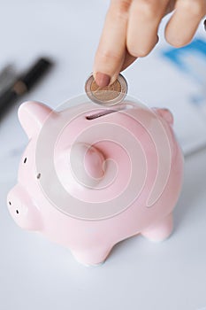 Woman hand putting coin into small piggy ban