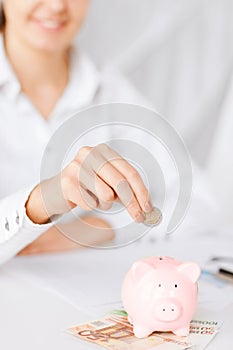 Woman hand putting coin into small piggy bank