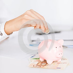 Woman hand putting coin into small piggy bank