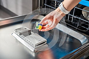 Woman hand putting detergent, multifunction tablet into the dishwasher. Household chores, duties with a modern kitchen
