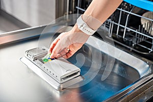 Woman hand putting detergent, multifunction tablet into dishwasher. Household chores, duties with modern kitchen
