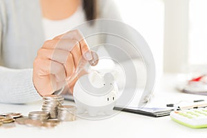 Woman hand putting money coin into piggy bank with stack of coin