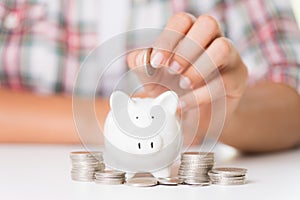 Woman hand putting money coin into piggy bank and stack of coins