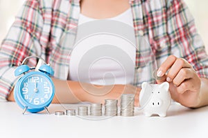 Woman hand putting money coin into piggy bank and stack of coins