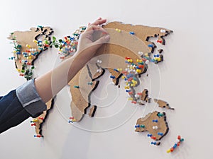 Woman hand putting red pin and marking location at wooden world map