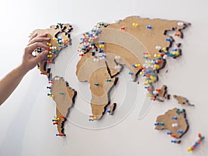 Woman hand putting red pin and marking location at wooden world map