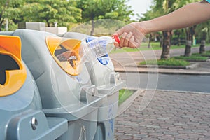Woman hand putting used plastic bottle in public recycle bins or segregated waste bins in public park.