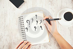 Woman hand question mark  on notepad and phone with coffee on table