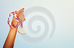 Woman hand raised, holding gold medal against sky. award and victory concept