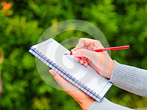 Woman hand with red pencil writing on notebook in agriculture garden.