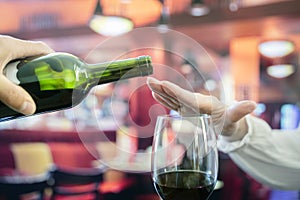 Woman hand rejecting more alcohol from wine bottle in bar