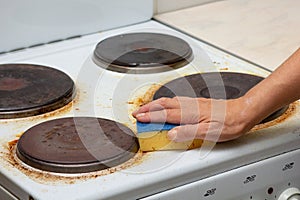 Woman hand remaining burnt stains on dirty electric stove scrubbing using sponge