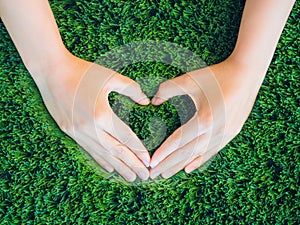 Woman hand in shape of heart on green grass background