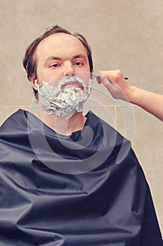 A woman hand shaves a man`s beard with a straight razor, close-up