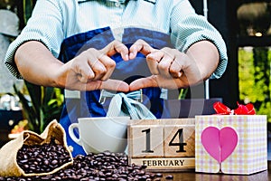 Woman hand show heart shap with gift box, 14 February wooden calendar, coffee cup and coffee beans. Valentine day concept photo