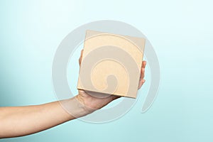 Woman hand show small brown rectangular cardboard box on light blue background. Mockup parcel box. Packaging, shopping