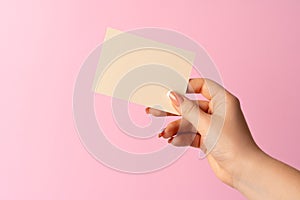 Woman hand showing blank business card on pink background.