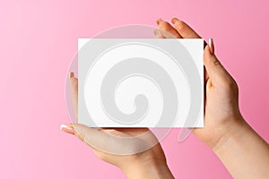 Woman hand showing blank business card on pink background.