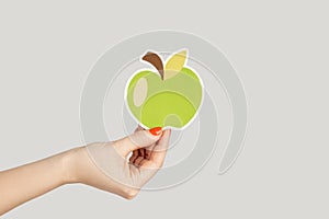 Woman hand showing paper green apple, symbol of healthy eating.