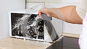 Woman hand spray detergent to outer surface of microwave. Housewife carry out wet cleaning of house. Clean home