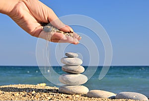Woman hand sprinkles sand on pebble stack
