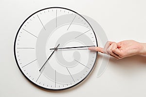 Woman hand stop time on round clock, female finger takes the minute arrow of the clock back, time management and deadline concept