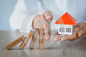 Woman hand stopping risk the wooden blocks from falling on house, Investment risk and uncertainty in the real estate housing