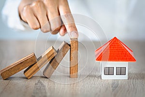 Woman hand stopping risk the wooden blocks from falling on house, Investment risk and uncertainty in the real estate housing