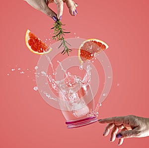 Woman hand support fly glass of grapefruit drink with splash, juice grapefruit slices falling in glass. Cocktail of grapefruit,