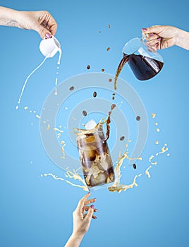 Woman hand support fly glass of tasty brew cold coffee and ice with splash, women hands is pouring homemade sour cream from small