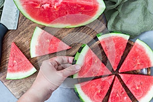 Woman hand take a slice of fresh seedless watermelon cut into triangle shape laying on wooden plate, flat lay, horizontal