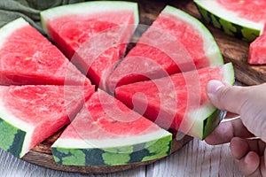 Woman hand take slice of fresh seedless watermelon cut into triangle shape laying on a wooden plate, horizontal