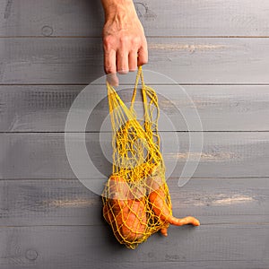 Woman hand takes eco friendly string bag with ugly carrot. Copy space