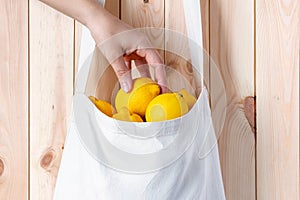 Woman hand takes a lemon from textile eco bag against wooden wall