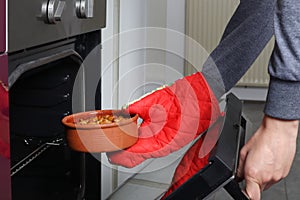 Woman hand takes it out terracotta saucepan with beans in the oven