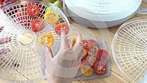Woman hand takes and puts slices of red and yellow tomatoes in the vegetable dryer on kitchen. Sun-dried tomatoes in a